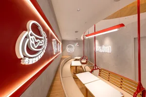 A minimalist restaurant interior with concrete walls, wooden seating, and neon lighting.