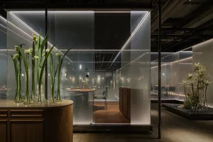 Modern restaurant with a glass privacy panel, featuring a wooden table setting and plants.