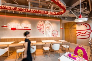 Modern fast food cafe with contemporary design elements, including wooden benches, white tables, and red lighting.