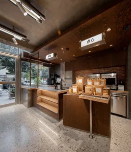 Interior view of an industrial-style restaurant with wooden elements, showcasing a counter, packaging bags, and a brick wall.