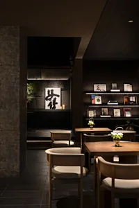 A modern cafe interior with wooden tables, fabric chairs, and concrete walls.