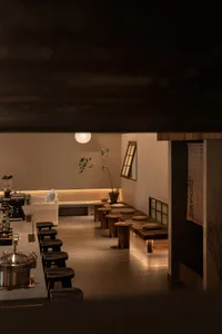 A minimalist restaurant interior featuring wooden furniture and a warm, inviting ambiance with soft lighting and a single pla