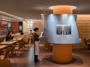 A minimalist restaurant interior with metal columns and cork walls, showcasing sleek design and functionality.
