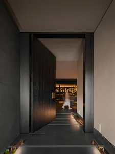 A modern minimalist entryway with a wooden door leading to a softly illuminated space.