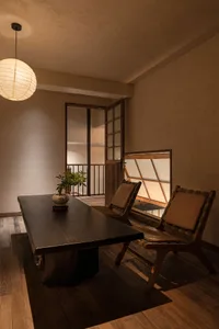 A modern minimalist office space featuring a wooden desk and chairs with a hanging lantern light.