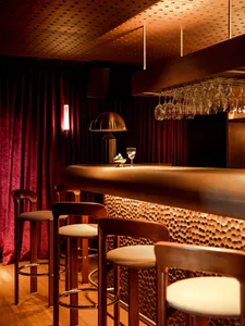 A modern restaurant bar with a wooden counter featuring lit up stools and hanging glasses.