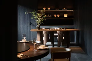 Modern restaurant interior with wooden tables, chairs, and dark, minimalist decor.