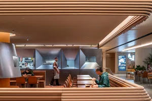 Interior shot of a modern restaurant with a concrete theme, featuring tables, chairs, and a view of the kitchen area.