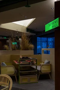 Modern cafe interior featuring wooden furniture, potted plants, and a green sign reading 'Serenity Hill'.