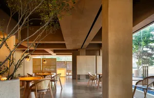A modern restaurant interior featuring concrete and wooden elements with potted plants.