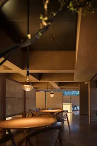 Modern minimalist restaurant with wooden tables and chairs, warm lighting, and natural elements.