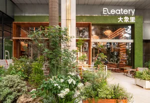 A modern casual cafe with green interiors, made from wood, stone, and glass, featuring a central table and chairs.