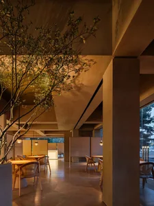 Modern restaurant interior with concrete walls, wooden furniture, and hanging lights.