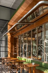 A modern cafe interior featuring wooden tables, glass windows, and green accents.