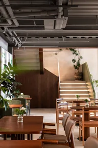 A cozy cafe interior featuring wooden tables and a staircase with plants.