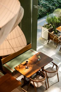 A modern cafe interior with minimalist furniture, wooden tables, and chairs with white cushions.