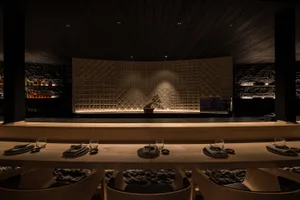 A modern restaurant interior with wooden tables and light-textured stone walls.