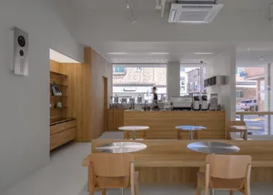 A cozy coffee shop with a wooden interior, featuring round tables and chairs, a counter with coffee machines, and a view of t