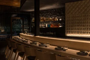 A minimalist restaurant bar interior with wooden seating and stone counter.
