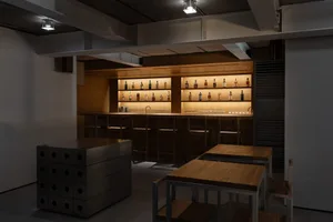 A modern bar counter with wooden surfaces and illuminated shelves showcasing various bottles of liquor.