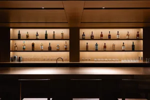 A modern bar counter with wooden shelves displaying various whisky bottles.