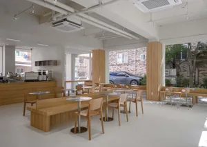 Modern cafe interior with wooden tables and chairs, white walls, and large windows.