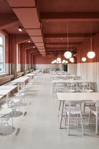 A spacious, modern cafeteria with multiple white tables and chairs arranged neatly in rows. The ceiling is painted in a warm 