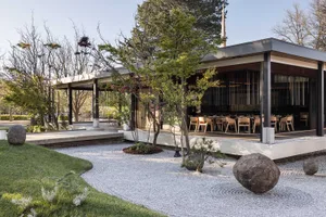 A modern restaurant exterior with wooden elements, featuring a pathway and trees.