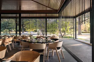 現代餐廳室內，混凝土地板、木質家具，以及可眺望綠意的大窗。
