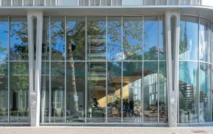 An exterior view of a modern restaurant featuring a glass facade with reflections of trees and the sky.