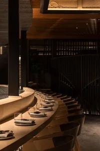 A modern restaurant interior featuring wooden tables and chairs arranged in a curved line, with soft lighting and a sleek des