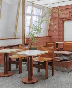 Modern restaurant interior featuring metal tables, leather chairs, cement flooring, and potted plants.