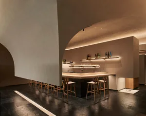 Modern, minimalist bar with concrete walls and wooden barstools, featuring a warm, inviting atmosphere.