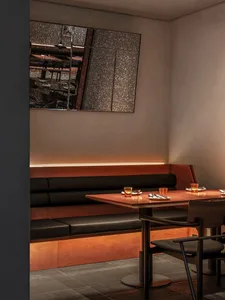 A cozy restaurant dining area with wooden tables and black-leather benches, featuring simple table settings and warm lighting