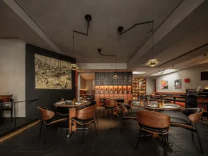 A modern restaurant interior featuring plush chairs with woven fabric upholstery, round tables with elegant tableware, and a 
