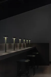 A minimalist bar with metal counters and wood stools under bright lighting.