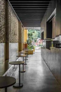 Minimalist cafe interior with concrete flooring, wooden stools, and green plants.