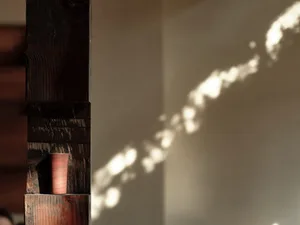Minimalist interior design featuring a wooden column and sunlight creating a shadow pattern on the wall.