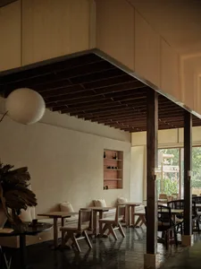A modern cafe interior featuring wooden tables and chairs, with a ceiling adorned with wooden beams.