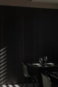 A modern dining room with dark wood walls and a small black table set for two, featuring two wine glasses and plates.