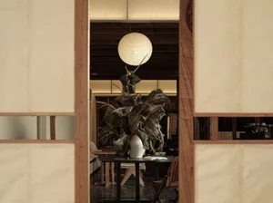 A modern restaurant interior featuring a wooden table with a decorative plant arrangement, and a spherical light fixture hang