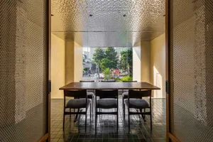 A modern dining room with a wooden table and chairs in front of a large window showing an urban street view.