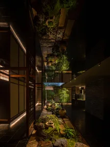 A serene corridor with concrete walls and green foliage, illuminated by soft lighting.