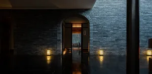A dimly lit lobby with a dark brick wall and floor, featuring a table and chairs in the distance.