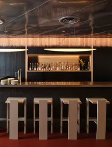 A sleek, modern bar counter with a wooden composite design, featuring a shelf with bottles and a minimalist stool arrangement