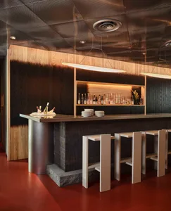 A modern bar with wooden walls and stools, featuring a counter with bottles and plates.