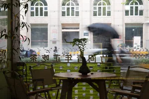 A cozy coffee shop with glass doors, wooden tables, and chairs, viewed from inside.