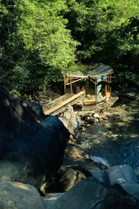 A wooden and netted structure built along a rocky stream in a forest.