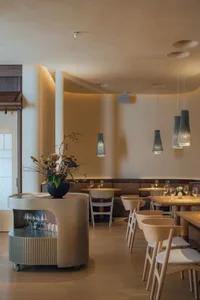 A modern restaurant interior with white walls, wooden furniture, and hanging pendant lights.