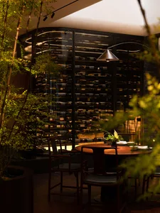 A modern wine bar featuring wooden furniture and a wine cellar with numerous bottles.